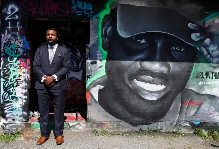 Lee Merritt, a lawyer representing the Arbery family, poses for a photo by a mural in the likeness of Ahmaud Arbery in Dallas – Photo by Tony Gutierrez / AP